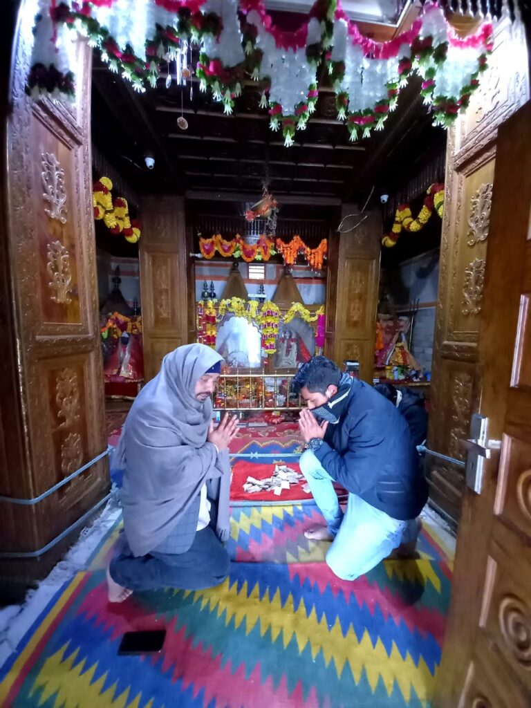 Two people kneeling in prayer on a colorful carpet in a richly decorated wooden shrine.